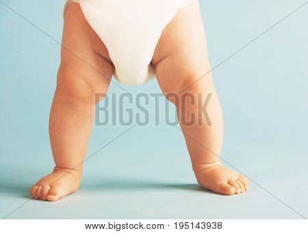 Low section of baby boy in diaper standing isolated on blue background