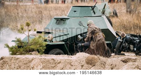 Gomel, Belarus - November 26, 2016: Re-enactor Dressed As Red Army Russian Soviet Infantry Soldier Of World War II Rescues Driver Crew From A Destroyed Armoured Soviet Scout Car At Battlefield During Historical Reenactment.