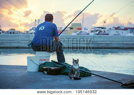 CYPRUS LIMASSOL - SEPTEMBER 22 2016: Local with cat fishing in the Limassol Old Port at sunset.
