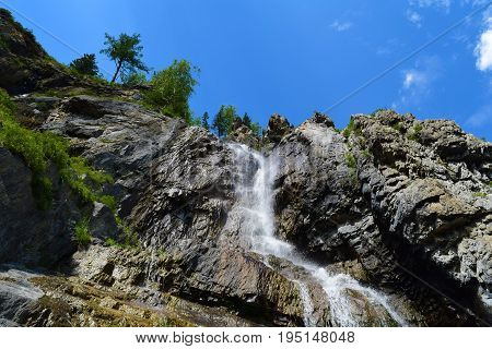 Landscape of Shirlak waterfall in rocks on blue sky with white clouds background. Tektu river Altai Mountains Altay Republic Siberia Russia.