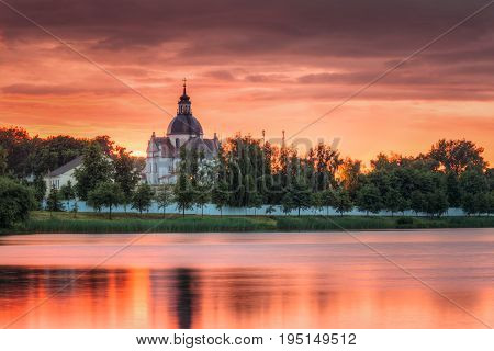 Nesvizh, Minsk Region, Belarus. Corpus Christi Church And Castle Pond Lake At Summer Sunset Evening Or Sunrise Morning. Famous Landmark In Nyasvizh.