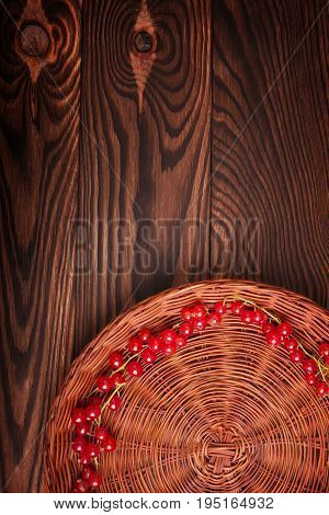 Close-up juicy red berries in the brown basket on a brown wooden background. Healthy bright red currant in a box. A basket full of delicious currant. Delicious bright red and mature currant.