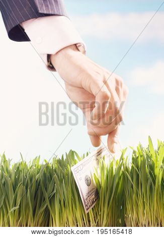 Closeup of a businessman picking up fifty dollar bill from grass against the sky