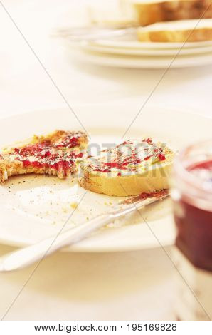Closeup of a plate with half eaten toast covered in jam on table set for breakfast