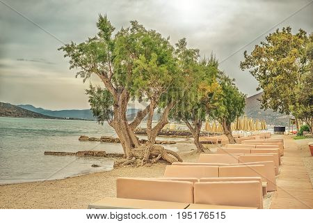 Dramatic landscape with a deserted sea beach with sun beds and juniper trees on the Gulf of Mirabello Greece Crete. Photo toned