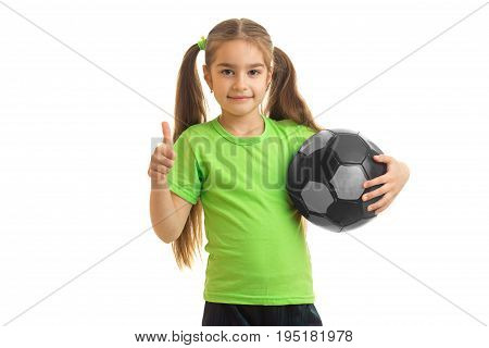 cheerful little girl with soccer ball in hands looking at the camera showing thumbs up isolated on white background