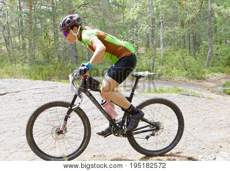 STOCKHOLM SWEDEN - JUNE 11 2017: Side view of female mountain bike cyclist in the forest on a rock at Lida Loop Mountain bike Race. June 11 2017 in Stockholm Sweden