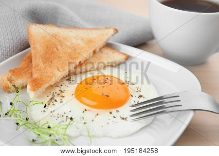 Plate of homemade over easy fried egg with toasts and cup of tea on table