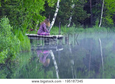 Young woman doing yoga exercises on the lake shore