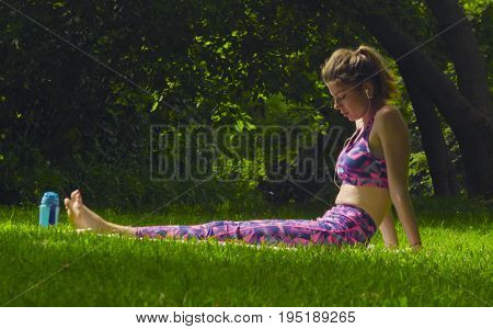 Young woman doing yoga exercises in the park. Akarna Dhanurasana