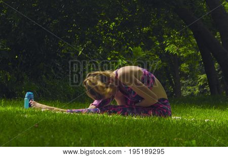 Young woman doing yoga exercises in the park. Akarna Dhanurasana. Pashchimotthanasana