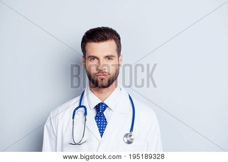 Portrait of handsome serious doctor in white coat and stethoscope on neck isolated on grey background