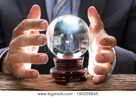 Midsection of businessman covering crystal ball at wooden table