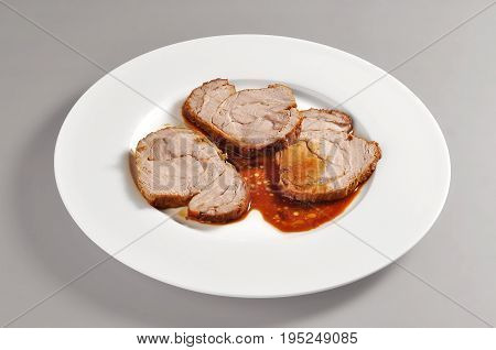 Plate with a portion of three slices of roasted veal portion on grey background