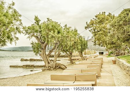 Deserted landscape with a deserted sea beach with sun beds and juniper trees on the Gulf of Mirabello Greece Crete. Photo tinted and styled
