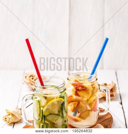 Two mugs of infused detox diet refreshing waters - first with cucumber and lemon, second with lemon and peach on white wooden table