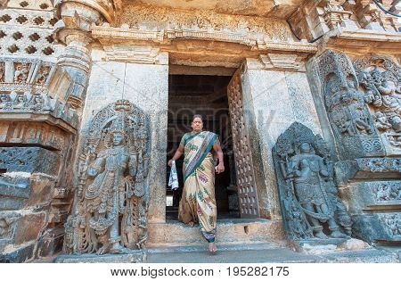 HALEBIDU, INDIA - FEB 22, 2017: Indian temple entrance and woman in sari coming past 12th century sculptures on February 22, 2017. Population of Karnataka is 62000000 people