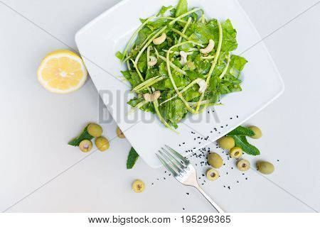Fresh salad with lemon. Fresh spinach salad with lemon and nuts on a white background on a white plate top view.