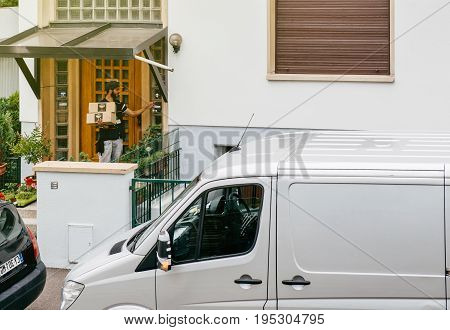 PARIS FRANCE - JUL 12 2017: Delivery worker man holding post parcel box knocking ringing at the doorbell and waiting the consignee to open the door and put the signature in clipboard