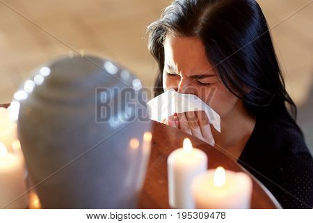 cremation, people and mourning concept - woman with wipe and cinerary urn crying at funeral in church
