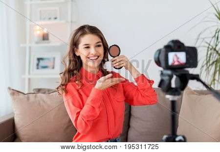 blogging, technology, videoblog, makeup and people concept - happy smiling woman or beauty blogger with bronzer and camera recording tutorial video at home