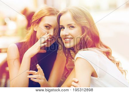 people communication and friendship concept - smiling young women drinking coffee or tea and gossiping at outdoor cafe