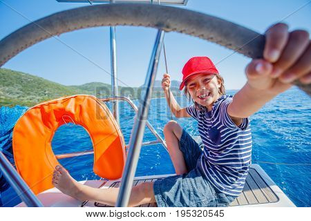 Cute boy captain on board of sailing yacht on summer cruise. Travel adventure, yachting with child on family vacation. Kid clothing in sailor style, nautical fashion.
