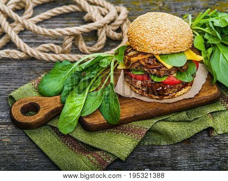 Big tasty hamburger with spices and herbs on wooden board and on table