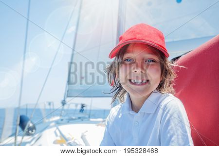 Cute boy captain on board of sailing yacht on summer cruise. Travel adventure, yachting with child on family vacation. Kid clothing in sailor style, nautical fashion.