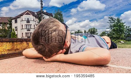 Playground relaxation, little boy looking at the blue sky in sung-lasses, lying on a table tennis table