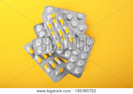 Shiny blisters with colorful white and yellow pills on a tellow background. Prescripted drugs in capsules. Antibiotics and painkillers in tablets. Medical treatment and pharmaceutical therapy.