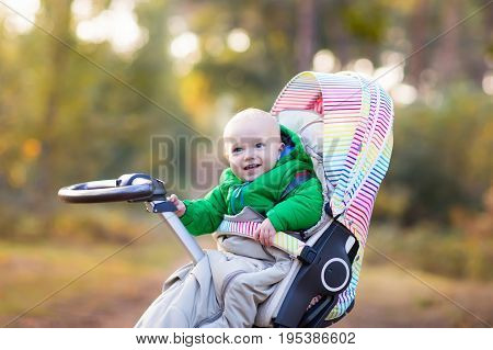 Baby in stroller on a walk in autumn park. Adorable little boy in green jacket sitting in colorful pushchair under warm blanket. Fall outdoor fun for kids. Child in buggy on winter stroll.