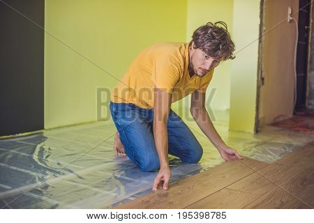 Man Installing New Wooden Laminate Flooring. Infrared Floor Heating System Under Laminate Floor