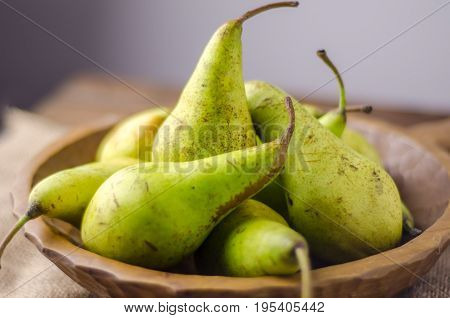 a bowl of green pears in a wooden bowl