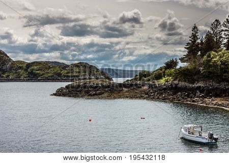 Assynt Peninsula Scotland - June 7 2012: Green rough forested hill slopes at Atlantic Ocean inlet South of Loch An Arbhair. Small white fishing boat. Stormy cloudy sky.