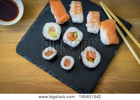 Sushi on a wooden table on black slate plate with soy sauce and chopsticks