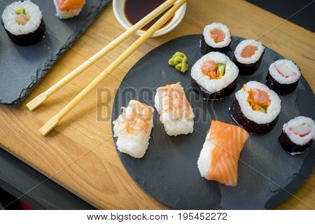 Sushi on a wooden table on black slate plate with soy sauce and chopsticks