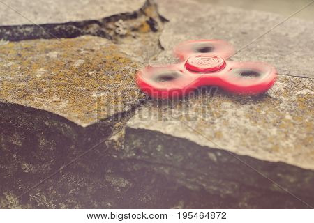 Red Spinner Fidget Toy Spinning On Stones Background. Toned.