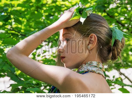 a young girl in a dress with nude backs worth in the foliage in the Woods hair decorated with foliage. in the sunlight.