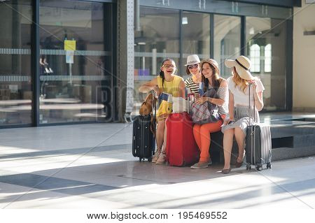 Cheerful girls at the airport waiting for flight. Young tourists briskly talk. In hands at girls of the passport and tickets. Summer vacation.