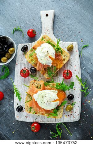 Poached egg on grilled toast with smoked salmon, rucola, olives and vegetables on white board. healthy breakfast.