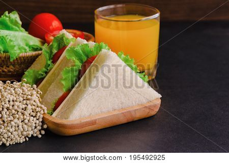Piece of sandwich ham cheese with lettuce and tomato on wood plate. Homemade sandwich served with orange juice for breakfast or lunch. Delicious ham cheese sandwich ready to served on granite table. Triangle slice sandwich ham and cheese.