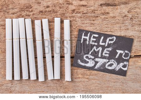 Group of cigarettes, paper message. White tobacco cigarettes, text help me to stop, old wooden background.