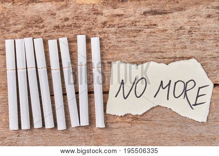 Tobacco cigarettes, message no more. White tobacco cigarettes and message lying on wooden background.