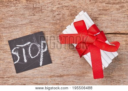 Pile of cigarettes with red bow. Tobacco cigarettes with red ribbon and message stop on wooden background.