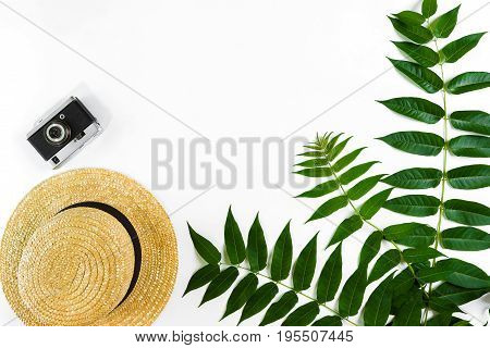 Straw hat with green leaves and old camera on white background, Summer background. Top view. Copy space. Still life. Flat lay