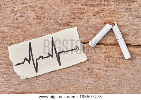 White tobacco cigarette broken. Broken tobacco cigarette, image of heartbeat, wooden background.