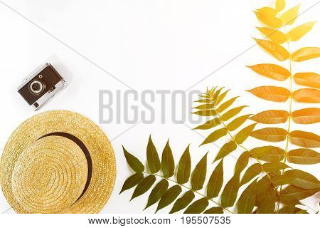 Straw hat with green leaves and old camera on white background, Summer background. Top view. Copy space. Still life. Flat lay. Sun flare