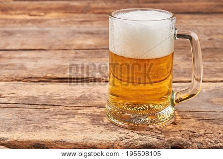 Glass mug with beer and foam. Full transparent glass of beer on old wooden background.