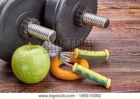 Healthy lifystyle concept. Dumbbells, green apple, expanders, wooden background.